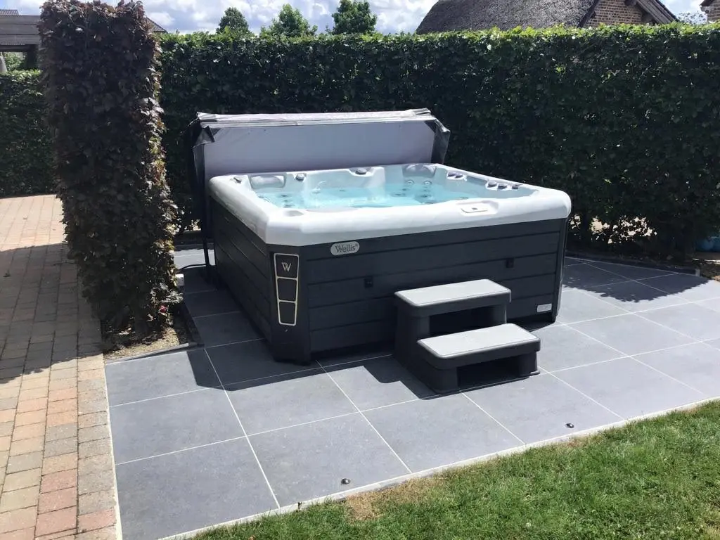 Wellis spabad op een bestrating in een verzorgde tuin